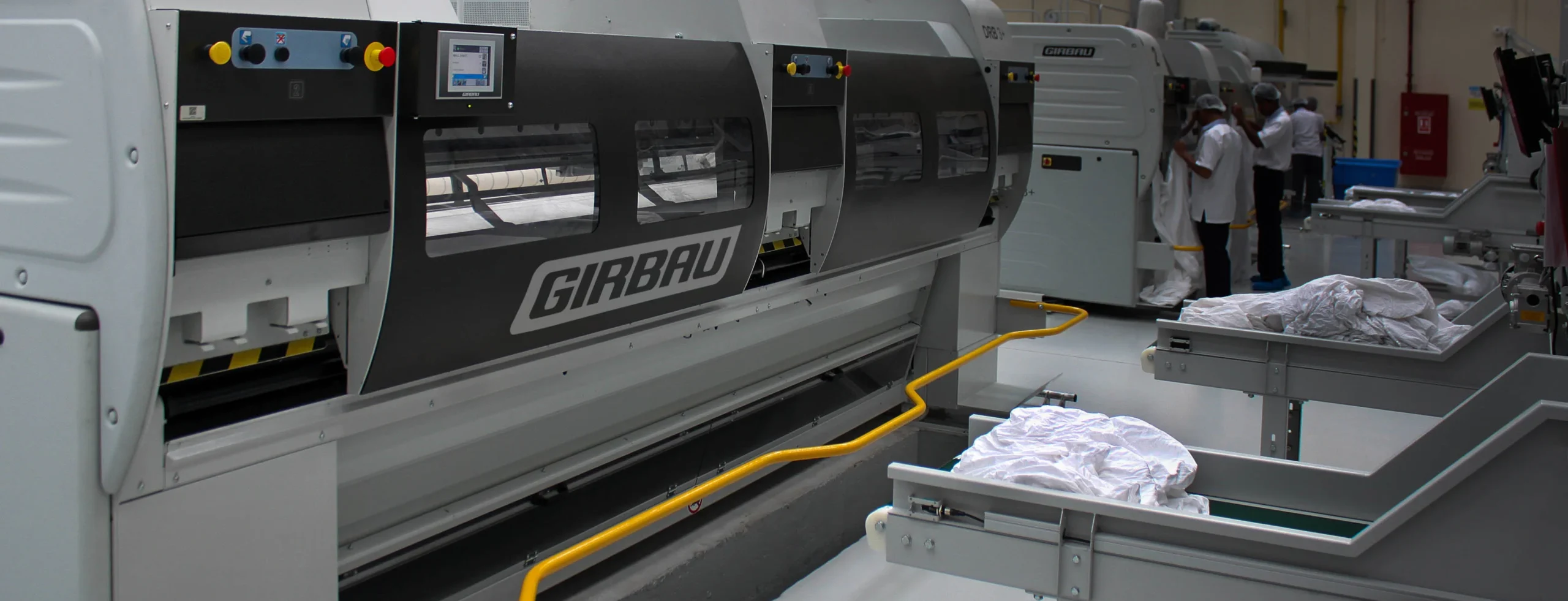 Industrial ironing line in operation with automated feeding, folding and finishing equipment, showing textiles being processed by high-efficiency flatwork ironers in a professional laundry.