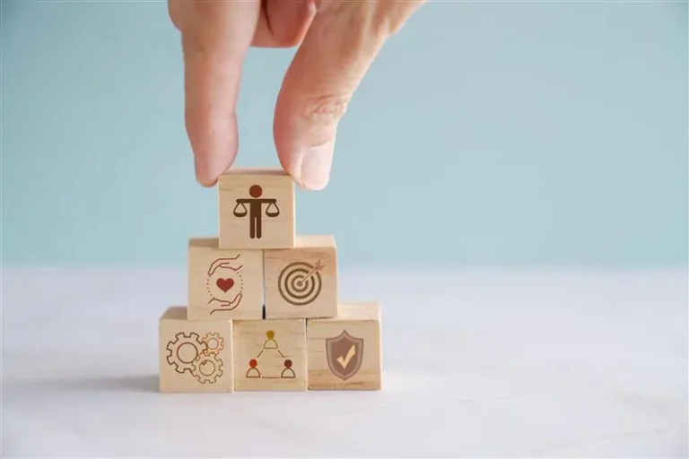 Hand placing wooden blocks with ethical and organizational values, representing Girbau’s Ethical Code based on integrity, transparency, and responsibility.