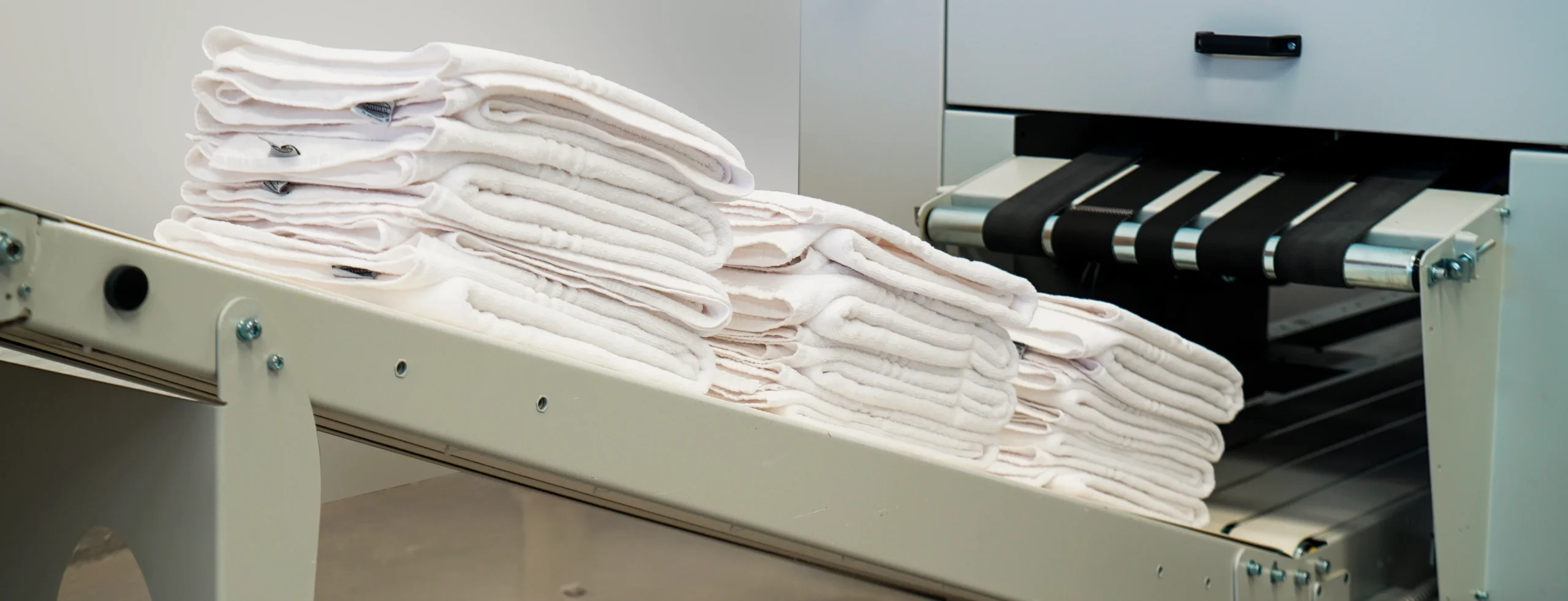 Automatic towel folding machine in operation, delivering neatly stacked towels for high-productivity laundry processes.