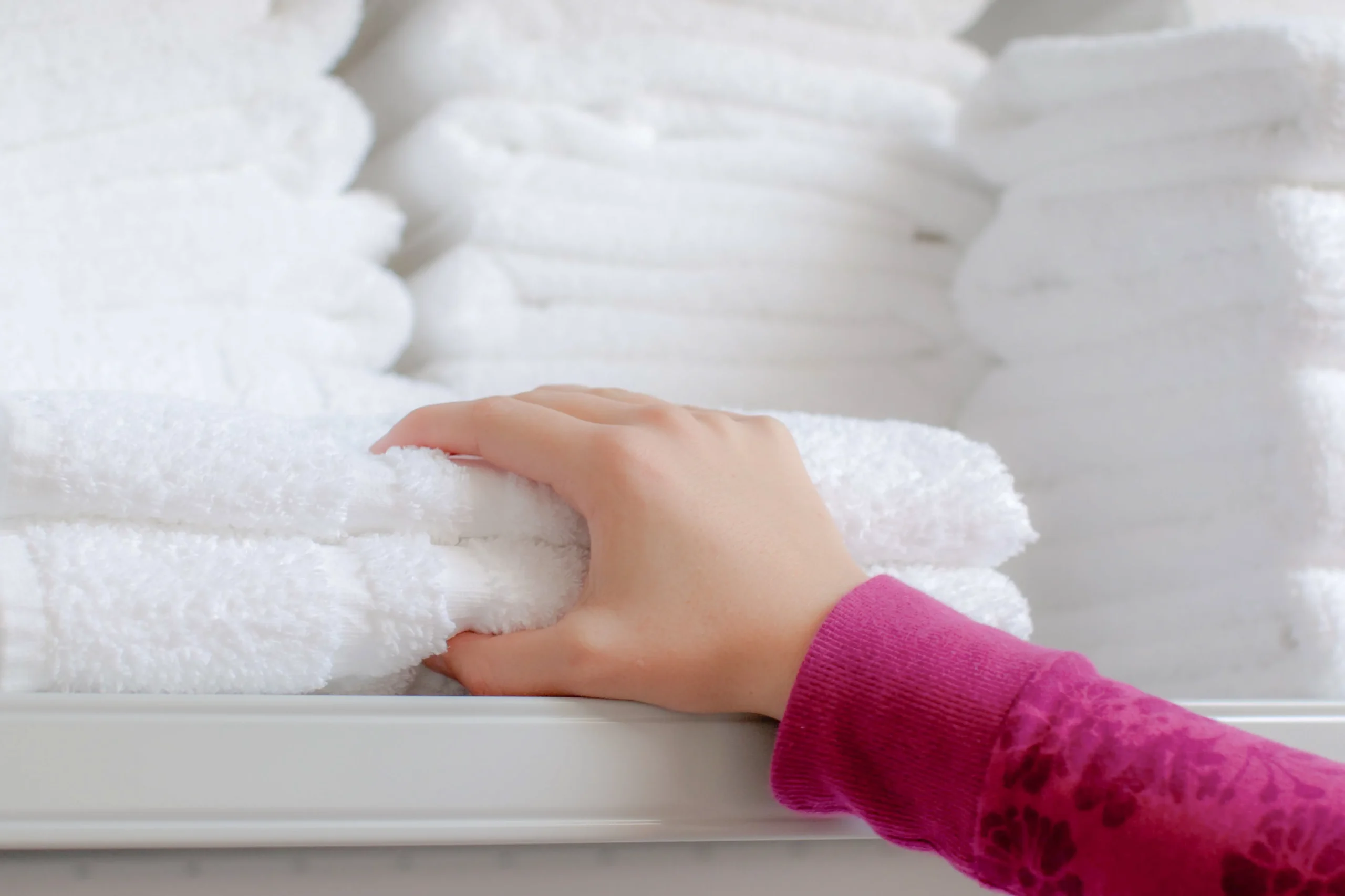 Hand selecting folded white towels from a storage shelf, representing hospitality laundry services for hotels and spas.