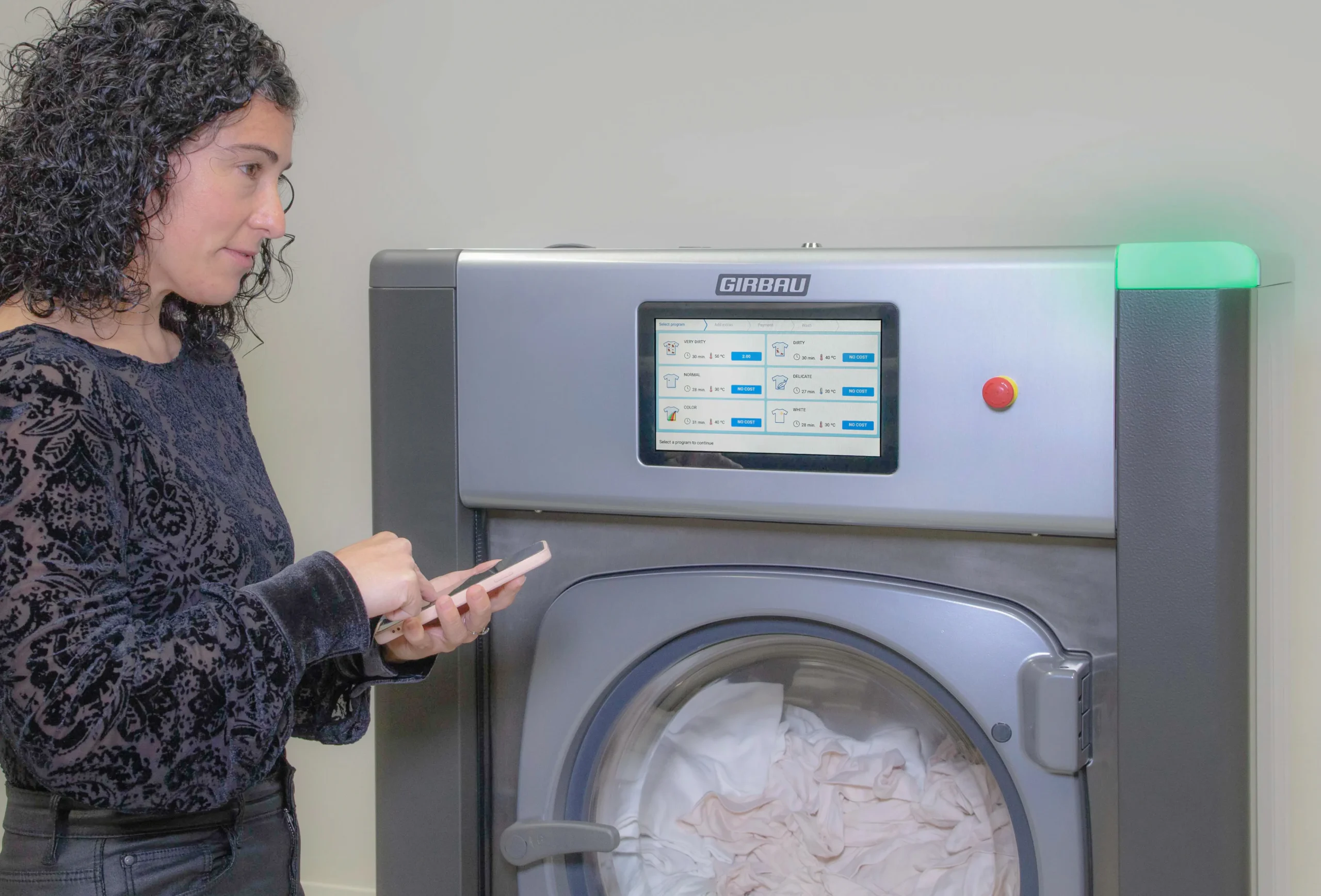 Woman operating a Girbau on-premise laundry washer with digital controls, representing laundry solutions for institutional and specialized facilities.