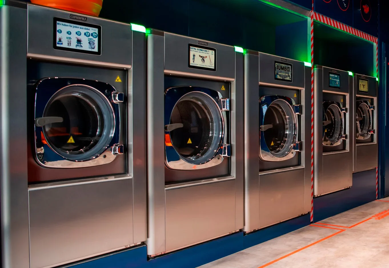 Row of industrial washing machines in a self-service laundry, showing Girbau commercial washers and efficient professional laundry equipment in daily use.