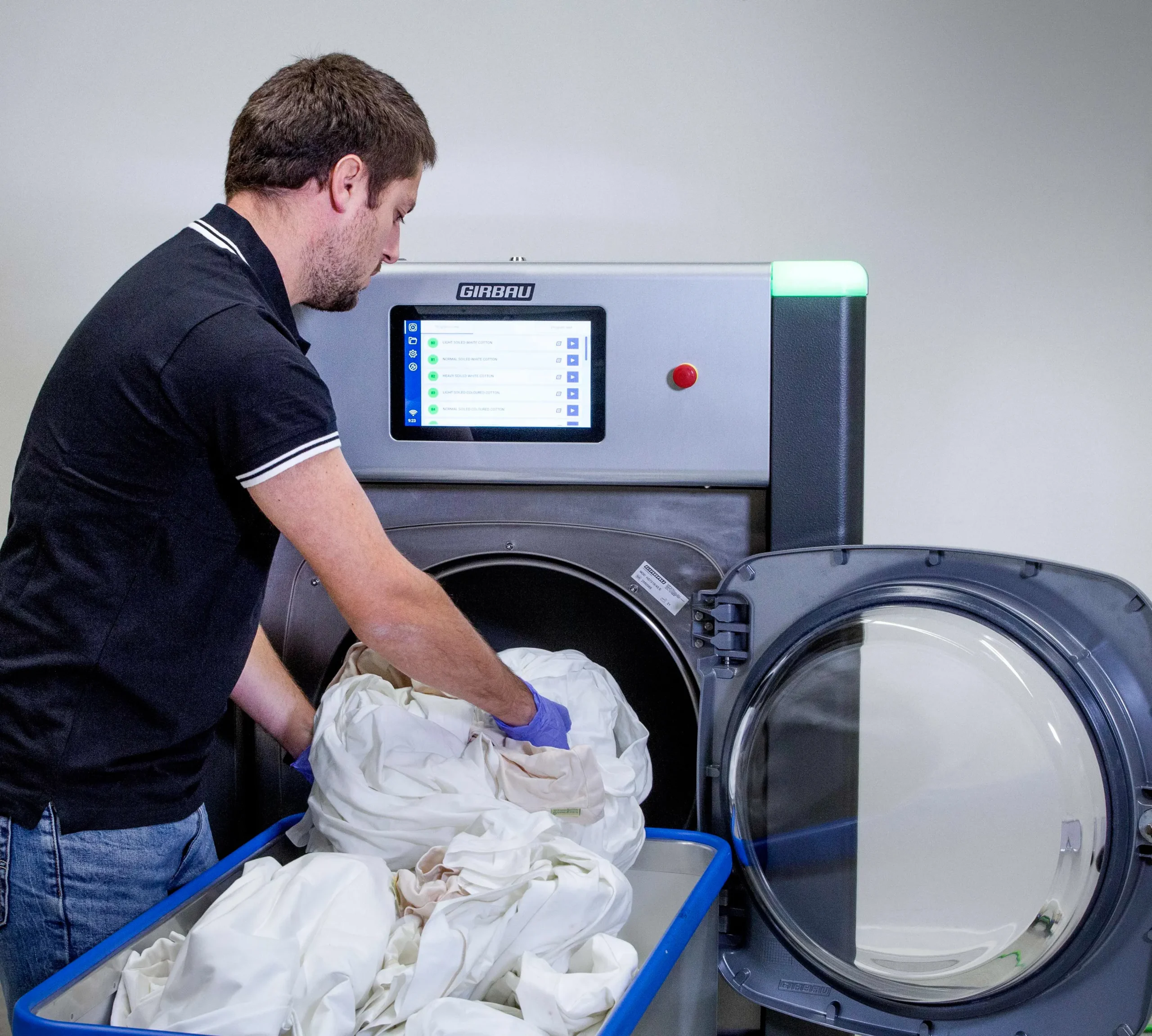 Operator loading white garments into a Girbau commercial washer, representing professional textile care and wet cleaning processes.