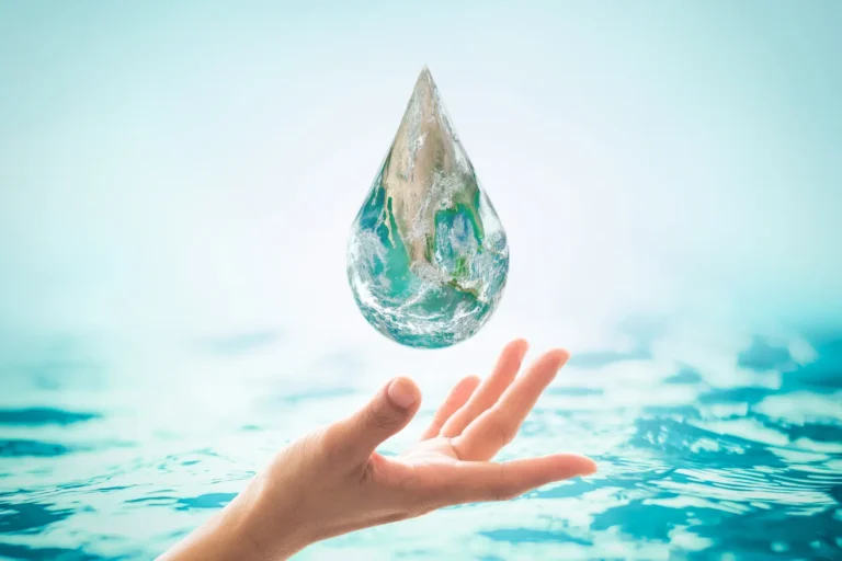 A water droplet showing planet Earth falling towards an open hand above clear blue water, symbolising water conservation.