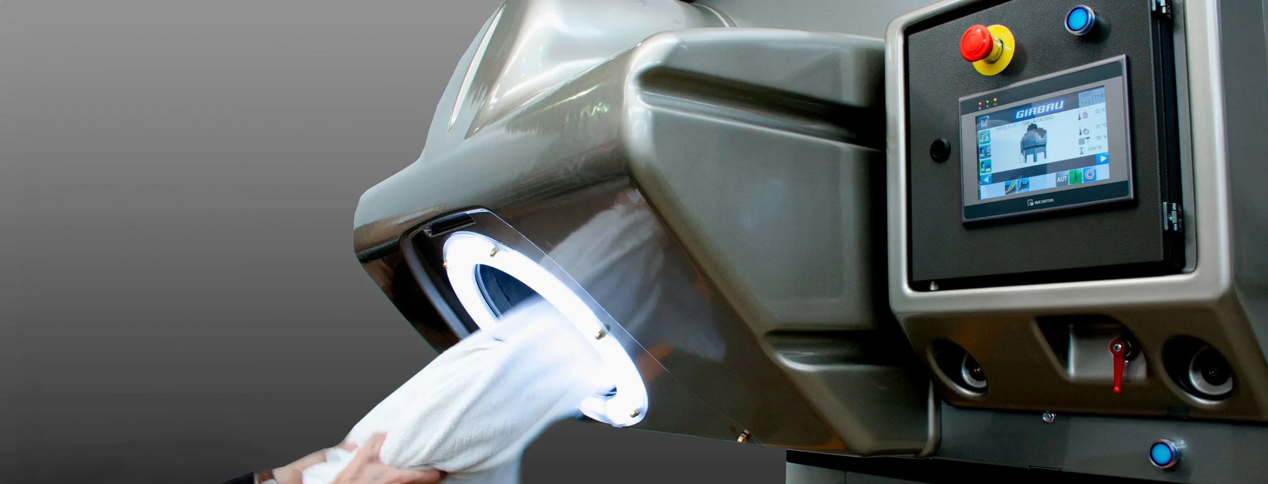 Màquina de secatge industrial expulsant aire calent mentre processa teixits, amb zona de càrrega il·luminada i panell de control avançat per a operacions de bugaderia de gran capacitat.