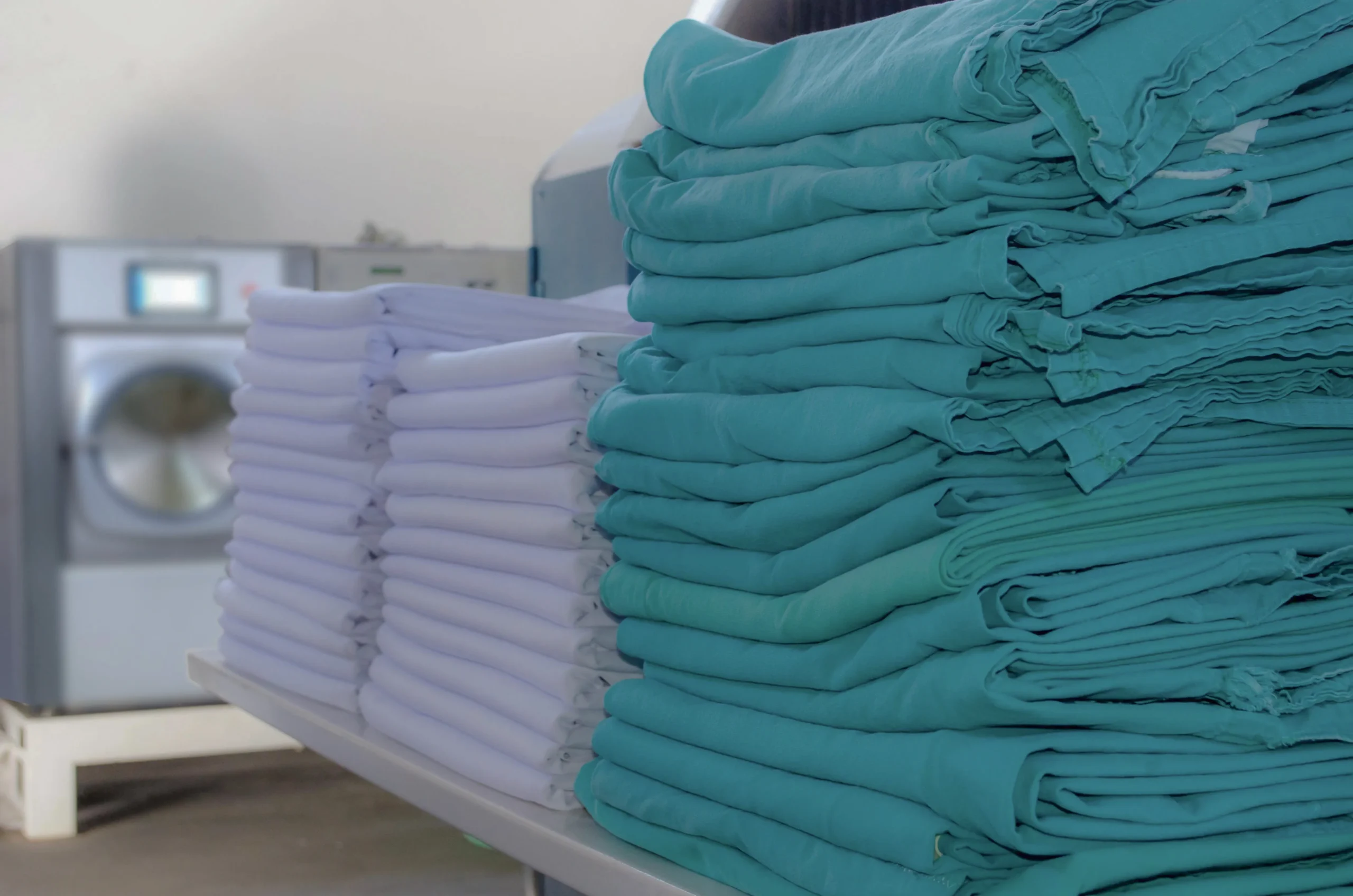 Pilas de ropa hospitalaria doblada lista para su distribución, mostrando eficiencia en las operaciones de lavandería sanitaria.