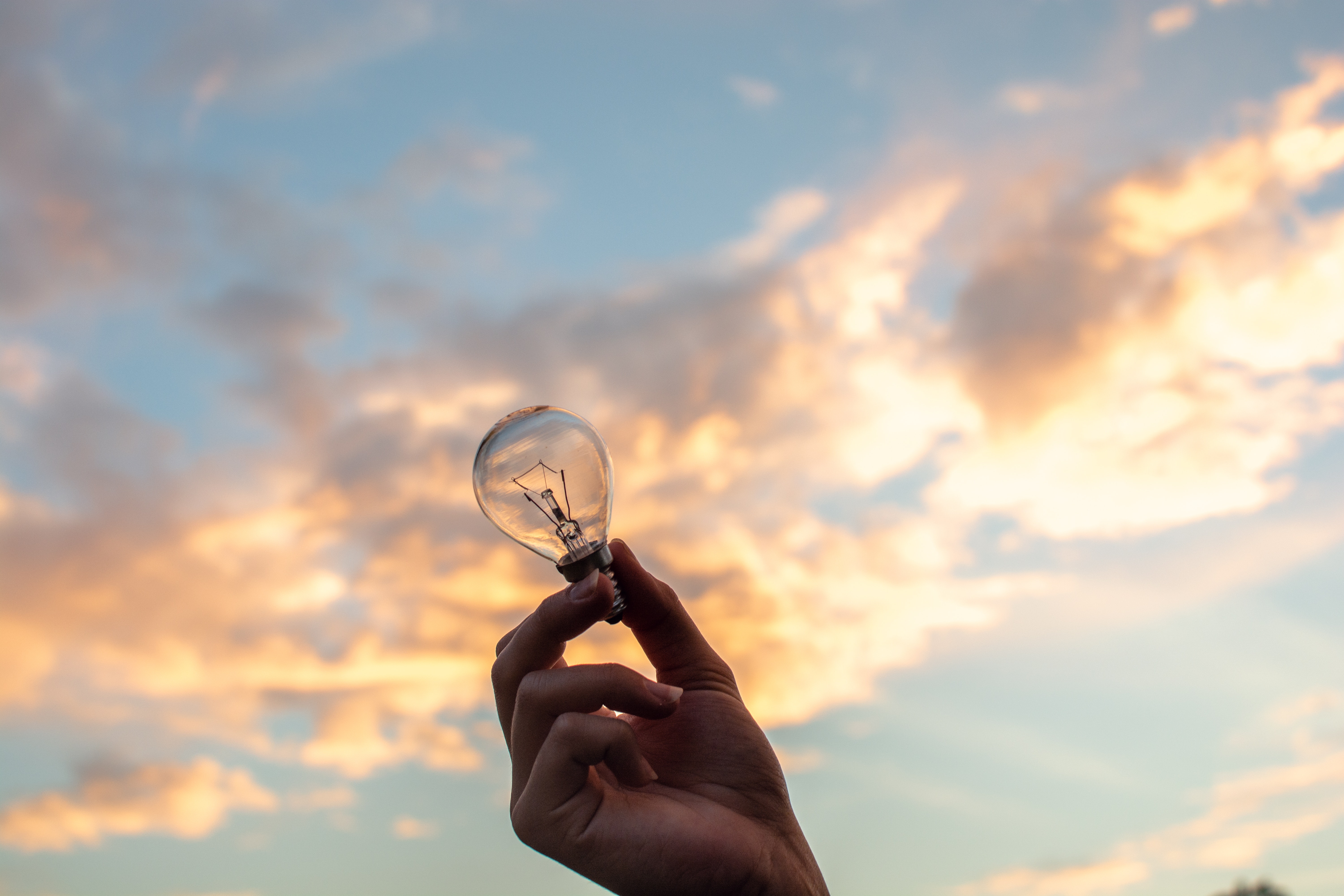 hand holding a bulb light with sky in the back