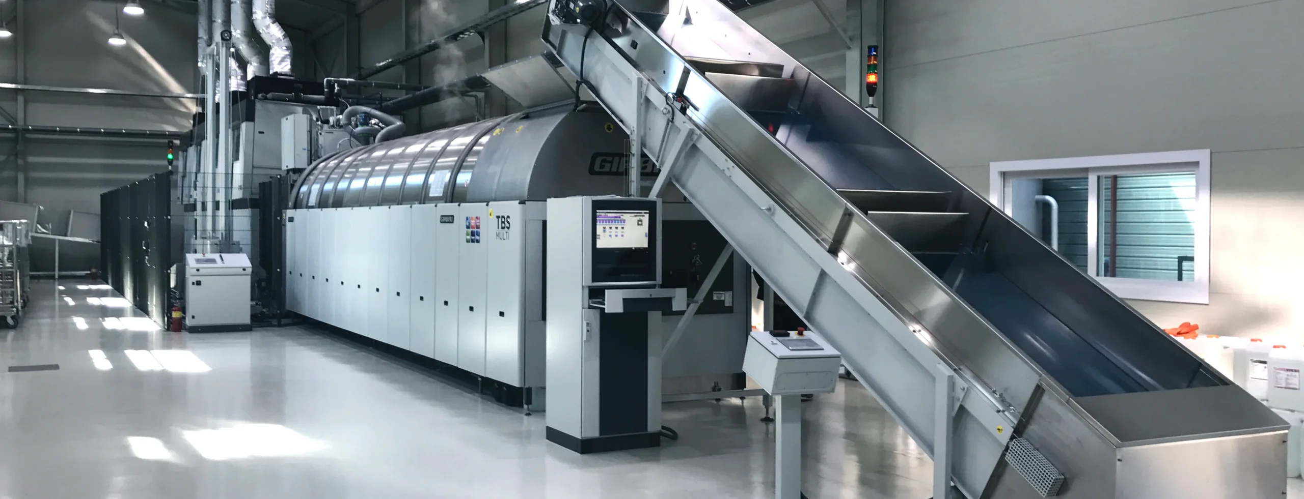 Sistema di lavaggio industriale a tunnel con caricamento automatizzato, illustrando processi di lavaggio continuo per lavatrici industriali ad alta capacità.