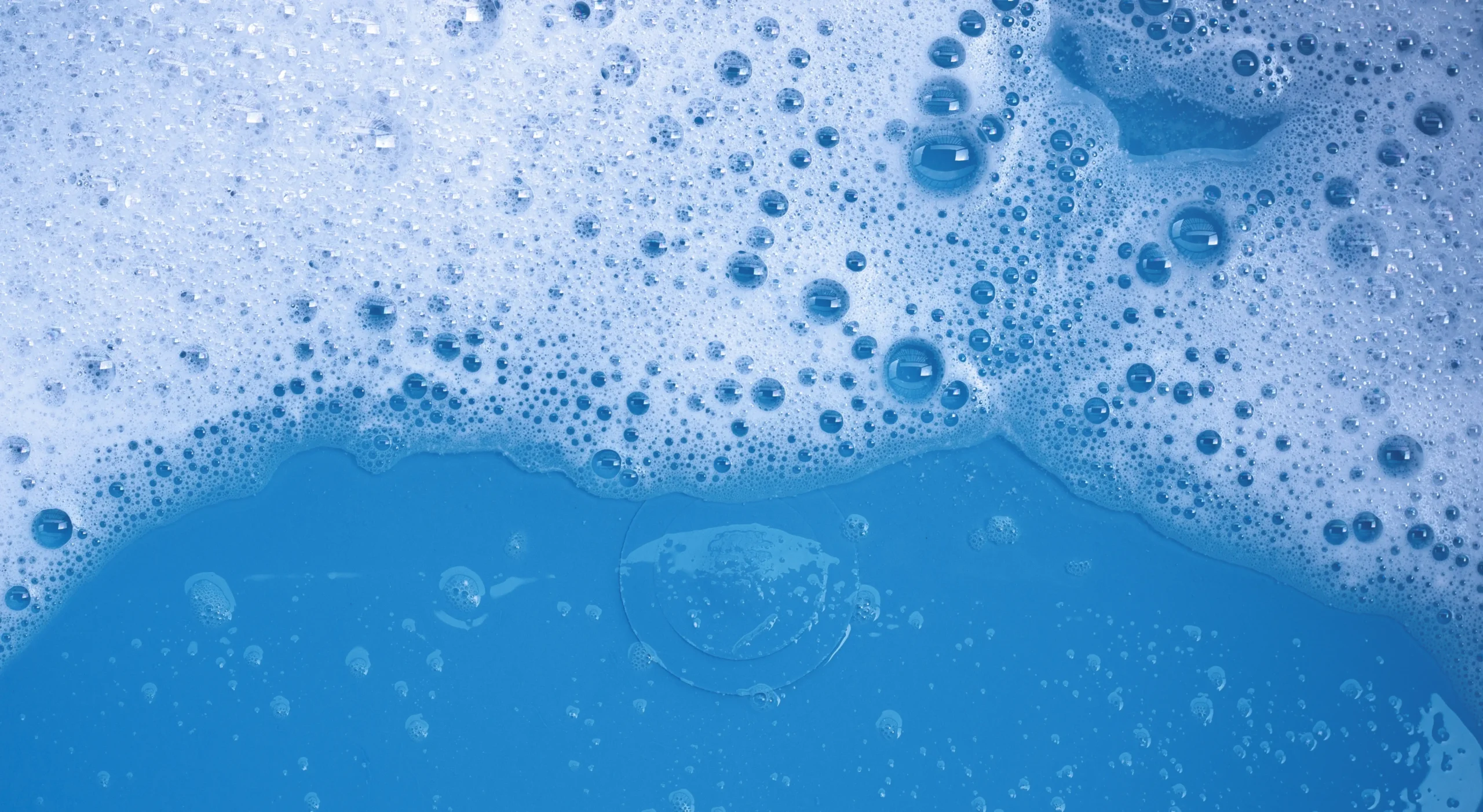 Close-up de espuma representando o sistema de dosagem automática de detergente da Girbau, projetado para aumentar a precisão, a eficiência e o controle químico em operações de lavanderia profissional.