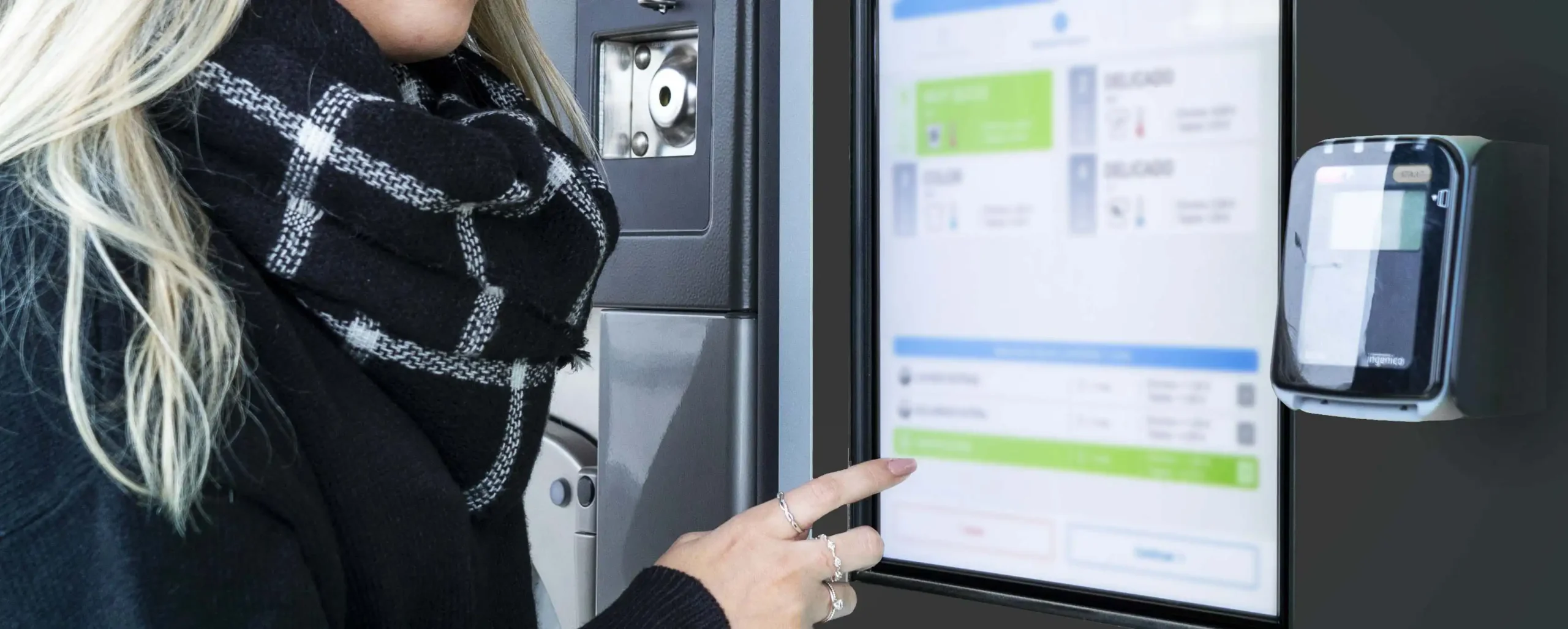 Cliente usando um totem de pagamento Girbau para lavanderia de autosserviço com interface touchscreen digital para transações rápidas e fáceis.