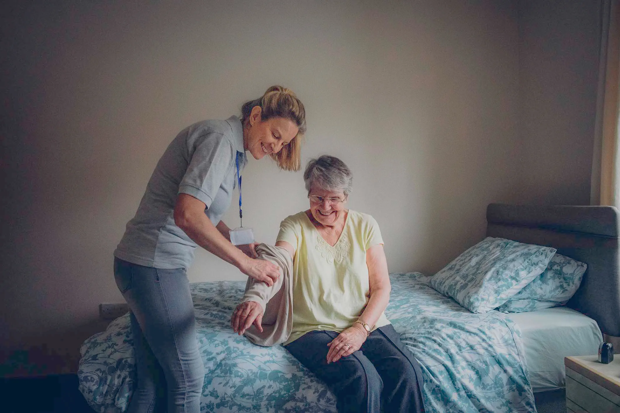 Caregiver assisting an elderly woman in a residential healthcare setting, illustrating the importance of hygienic and reliable laundry services.