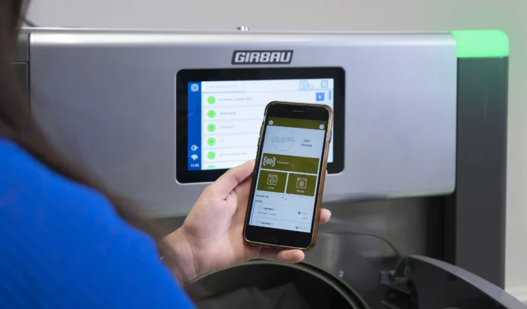 User managing a Girbau industrial laundry machine through a mobile app with smart digital connectivity.