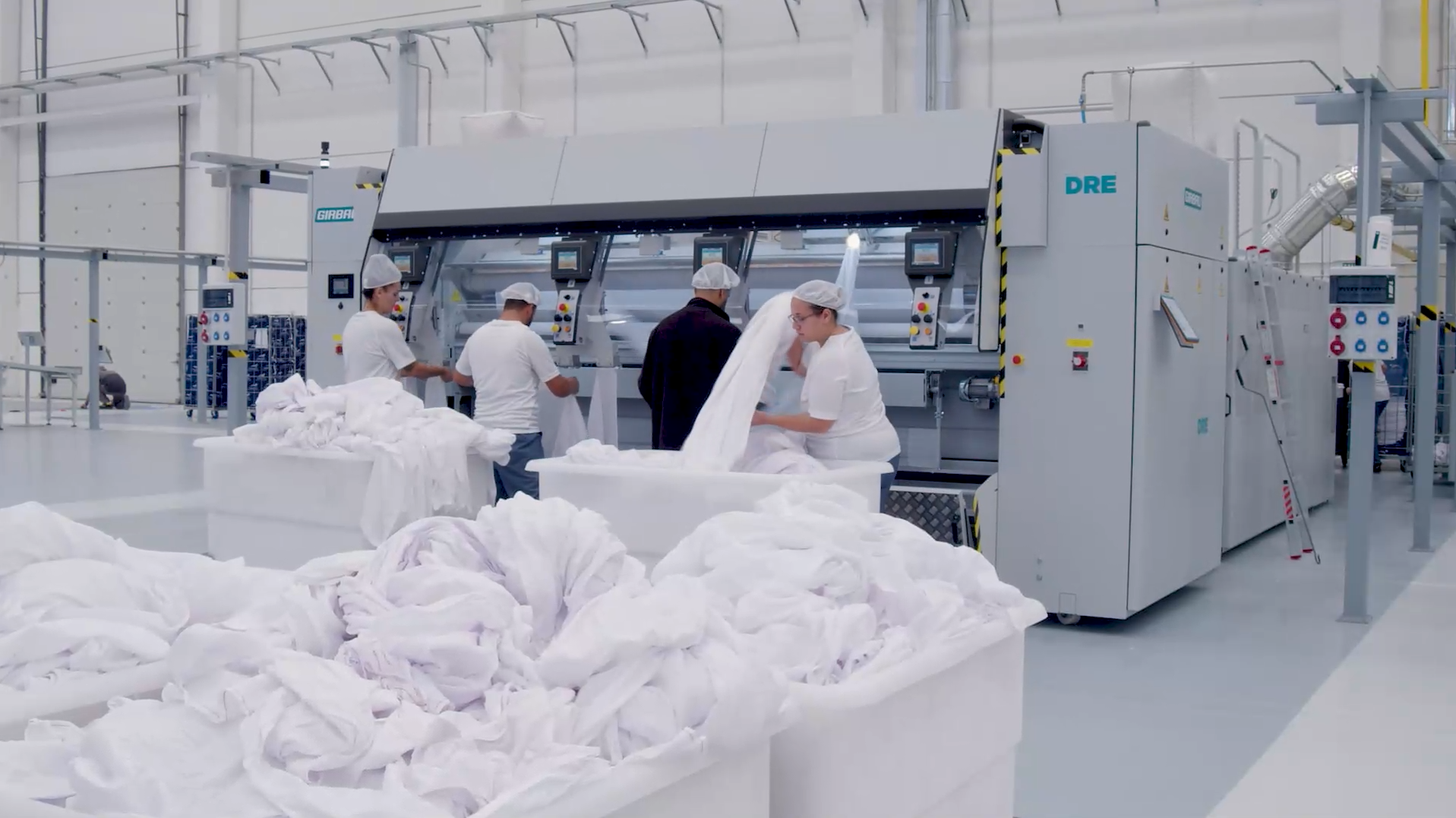 Industrial laundry team handling large volumes of white linens at a Girbau processing line, representing automated high-capacity laundry operations.