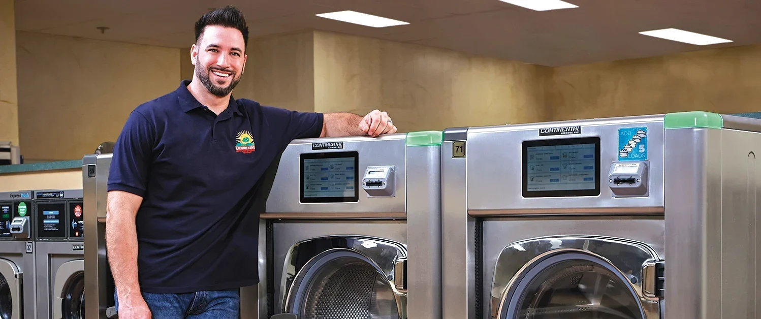 Owner’s son next to Girbau industrial washing machines in a self-service laundry.
