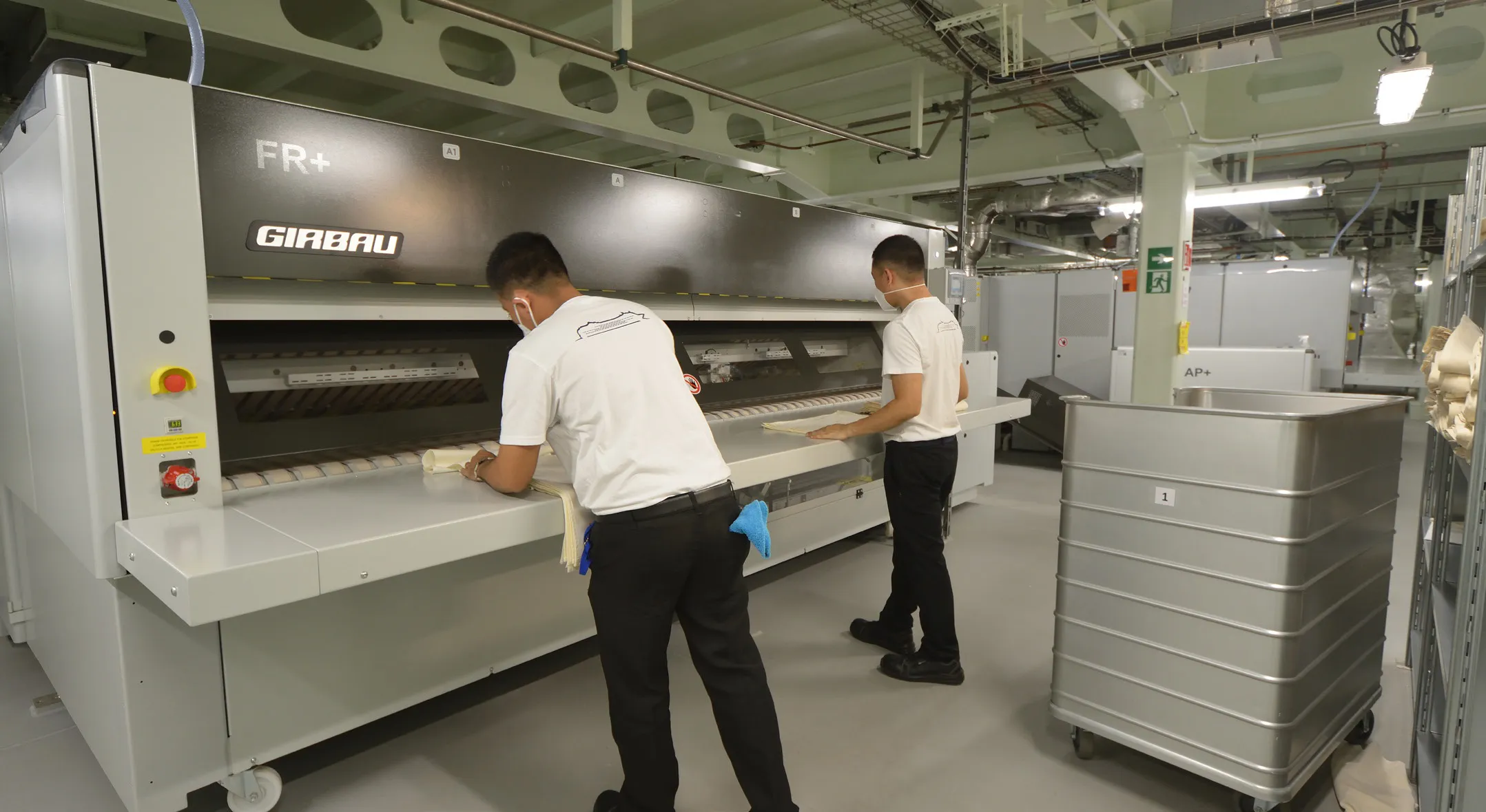 Staff operating a Girbau industrial ironing line onboard MSC World Europa, improving commercial laundry efficiency on cruise ships.