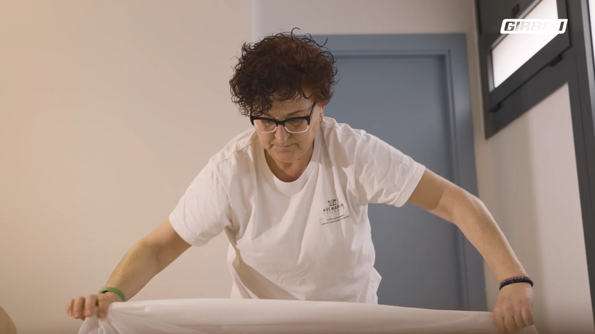 Staff member preparing a bed with clean sheets. 