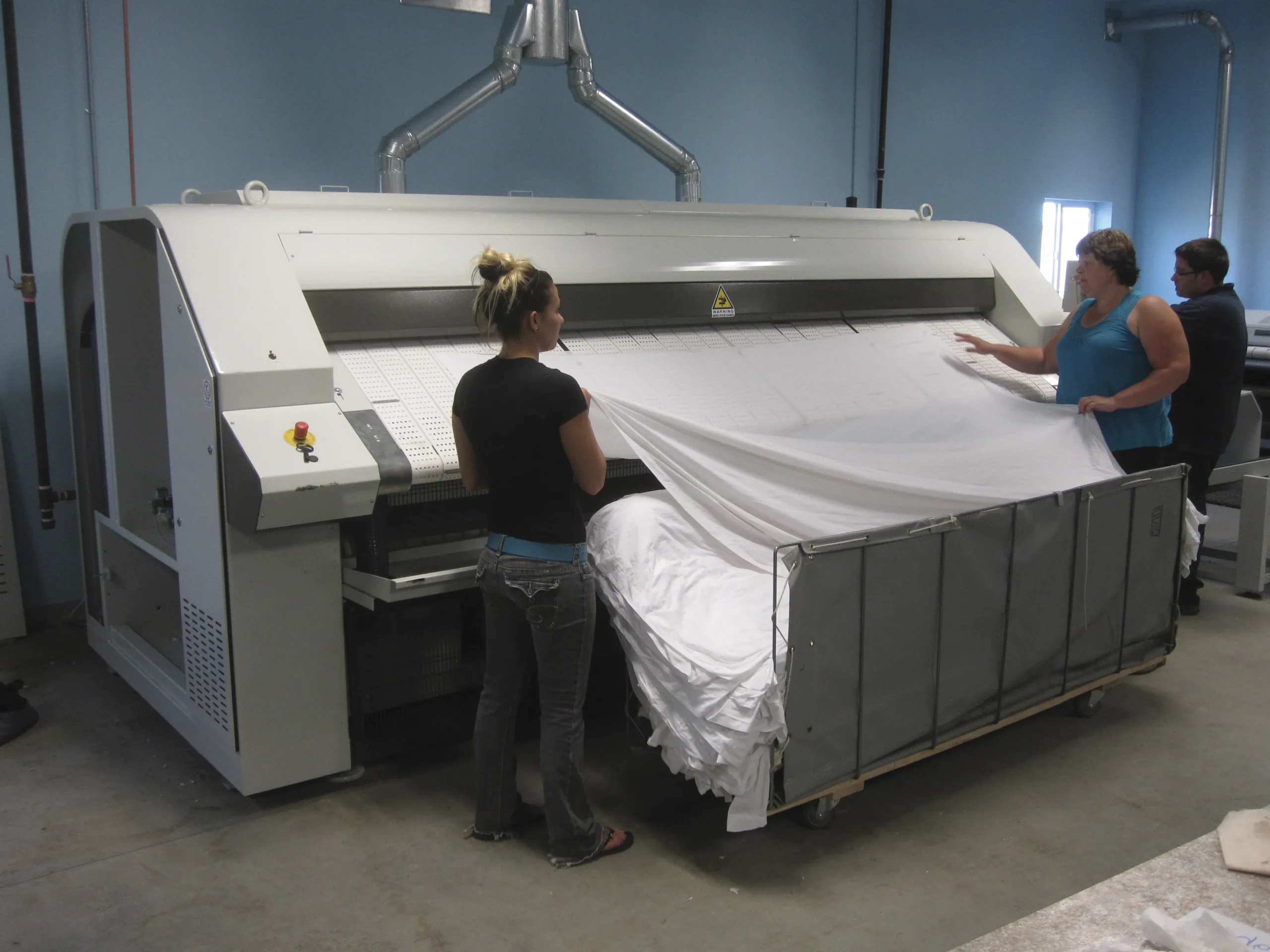 Operators using a Girbau flatwork ironer for linen finishing at Krazee Klean.